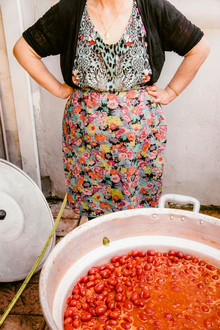 A woman in a floral apron stands by a large pot of cherry tomatoes.