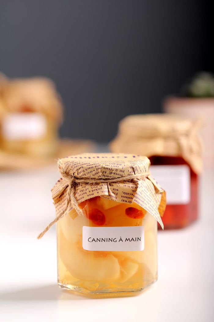 Close-up of homemade canned fruit jars in decorated containers on a wooden surface, showcasing artisanal preservation.
