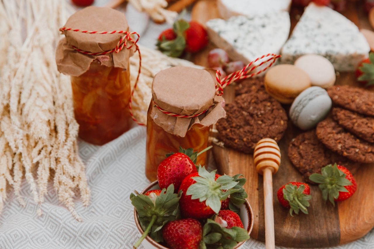 Delightful spread of homemade jam, strawberries, cheese, and cookies on a picnic table.